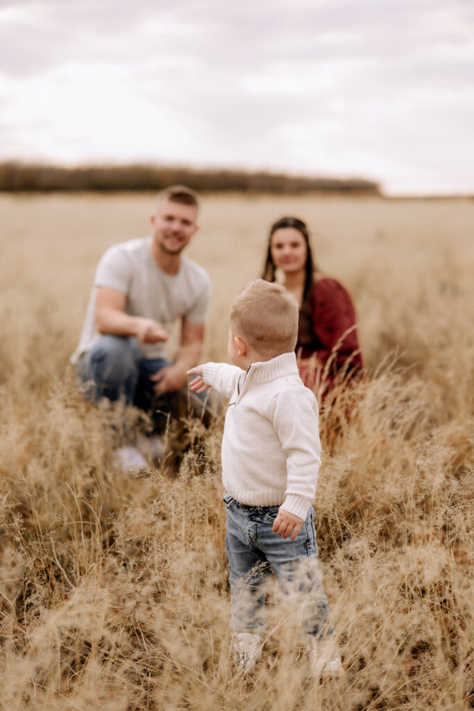 couple kneeling in open field with their son in front of them pointing