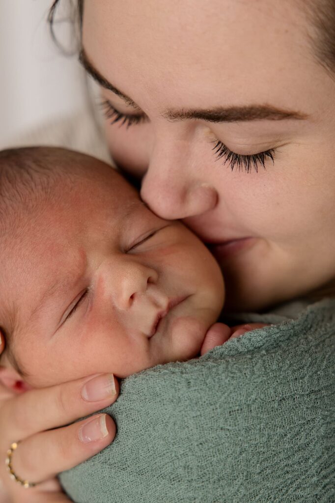 Mama holding baby boy kissing him on cheek during this studio newborn session.