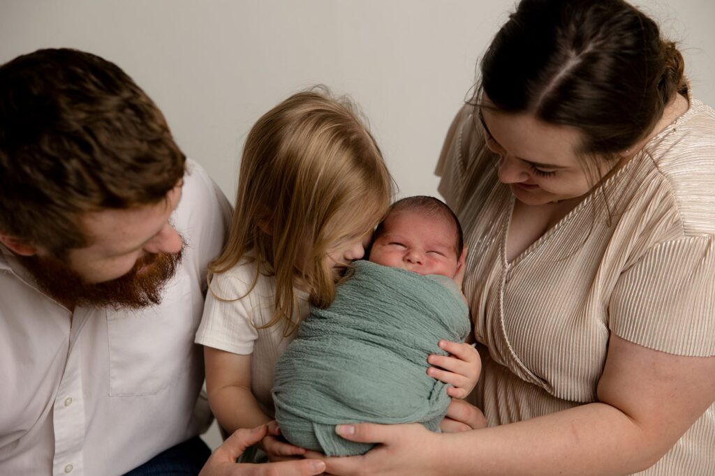 Family of 4 sitting holding their newborn baby.