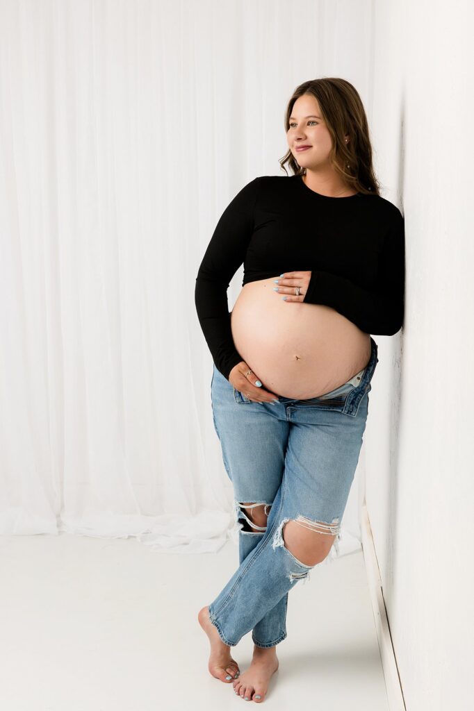Pregnant momma looking off of camera, holding her hands on her belly.