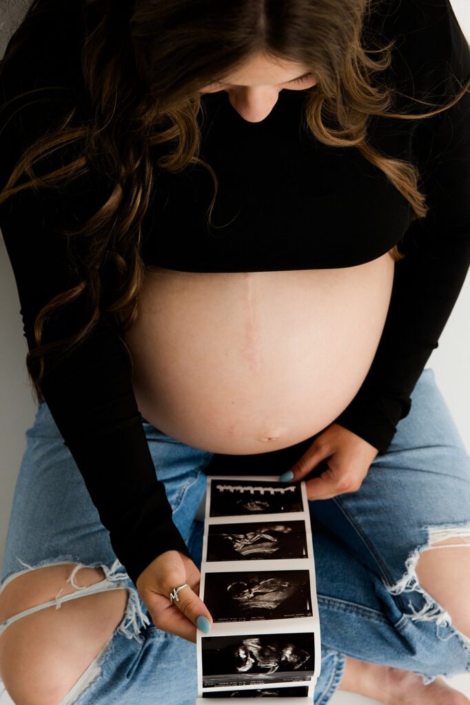 Pregnant momma looking at the sonogram paper while sitting on the floor.
