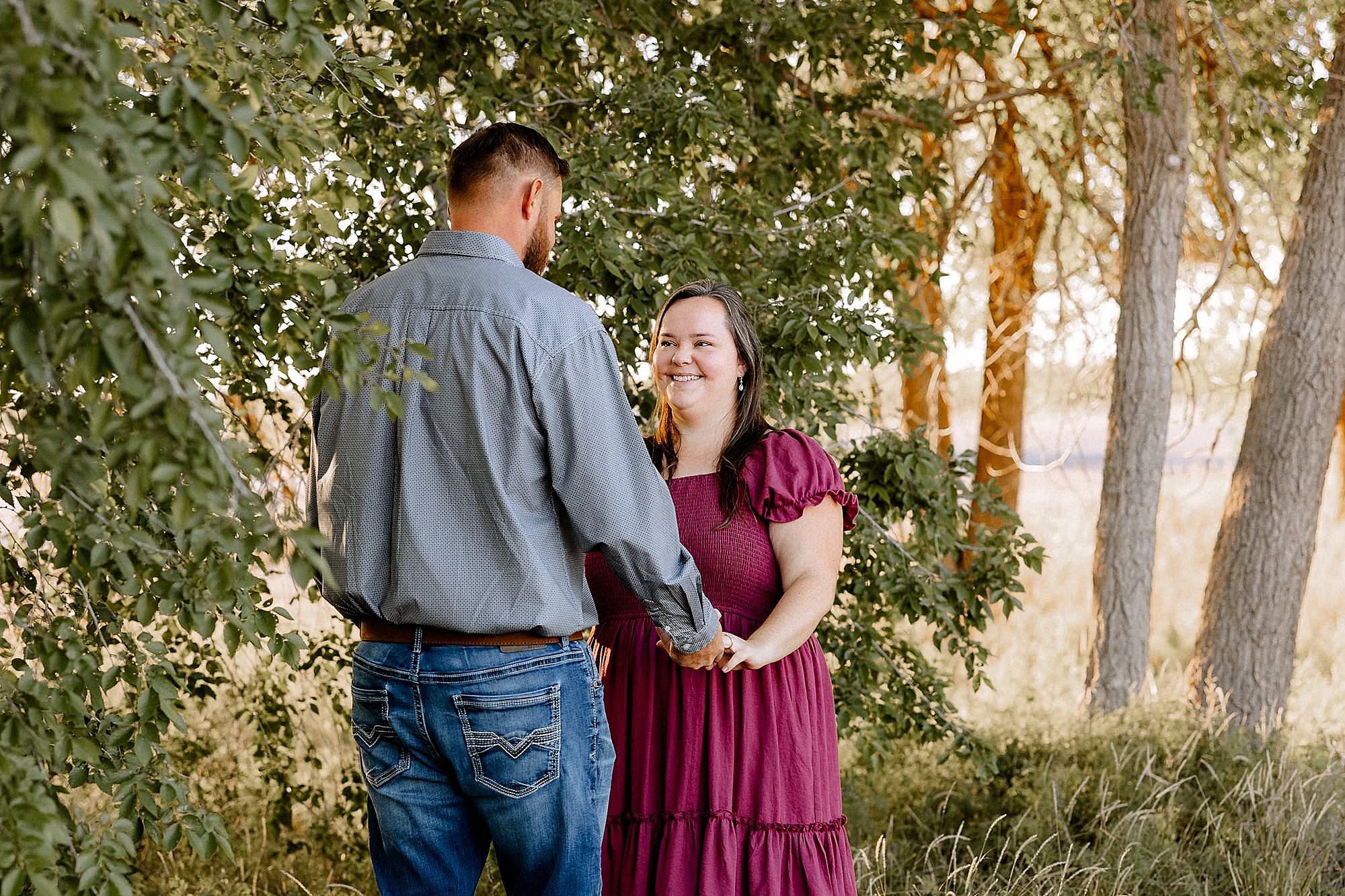 Couple holding hands during a mini session as the sun is shining through the trees behind them.