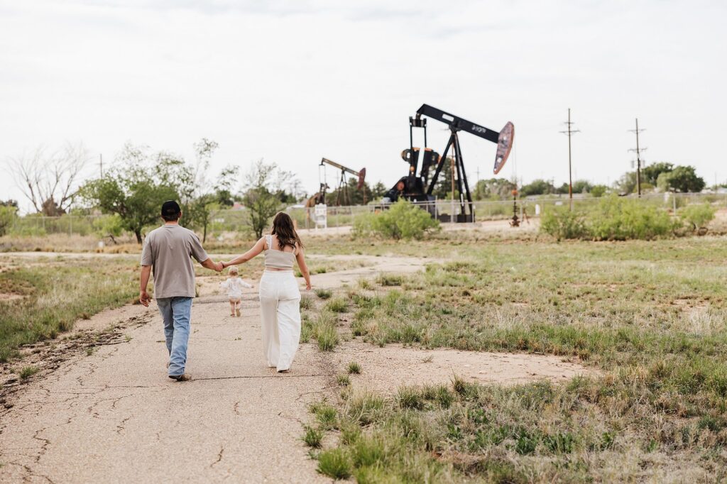 Husband and wife walking holding hands, their daughter is running ahead of them.