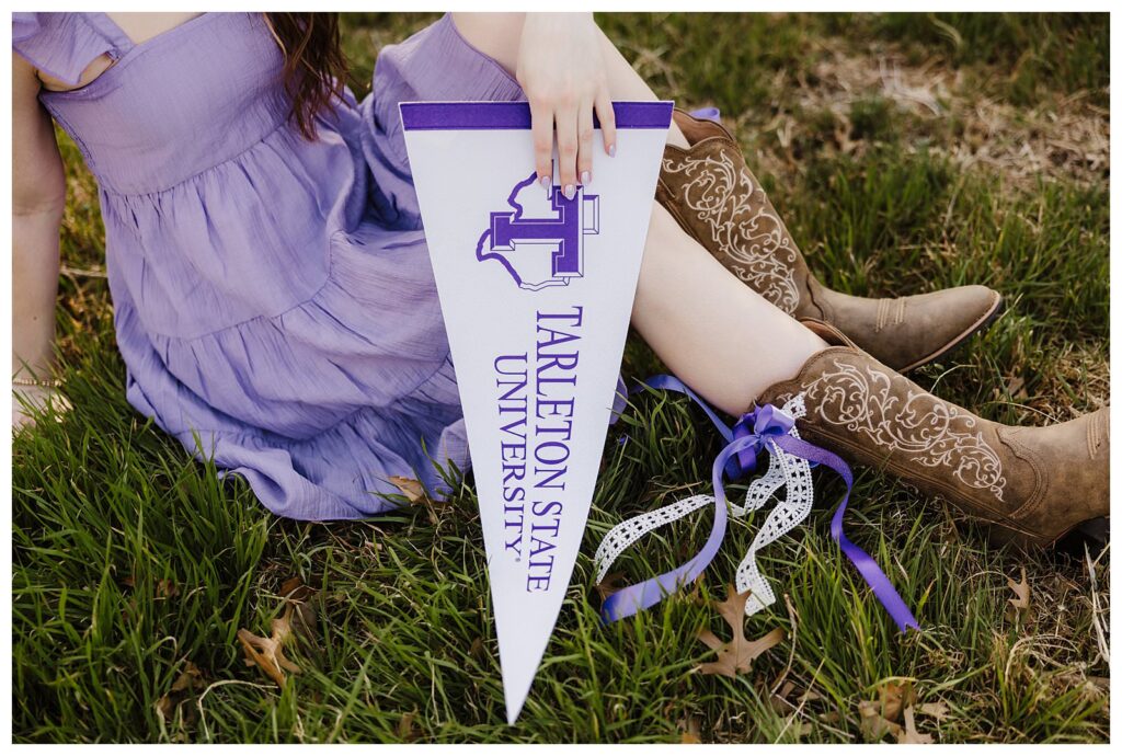 close up of senior girl in purple dress holding university sign while wearing cowgirl boots with purple bow 
