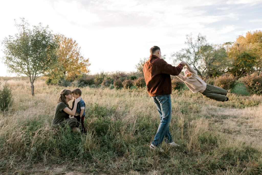 young couple playing with their children in a field.