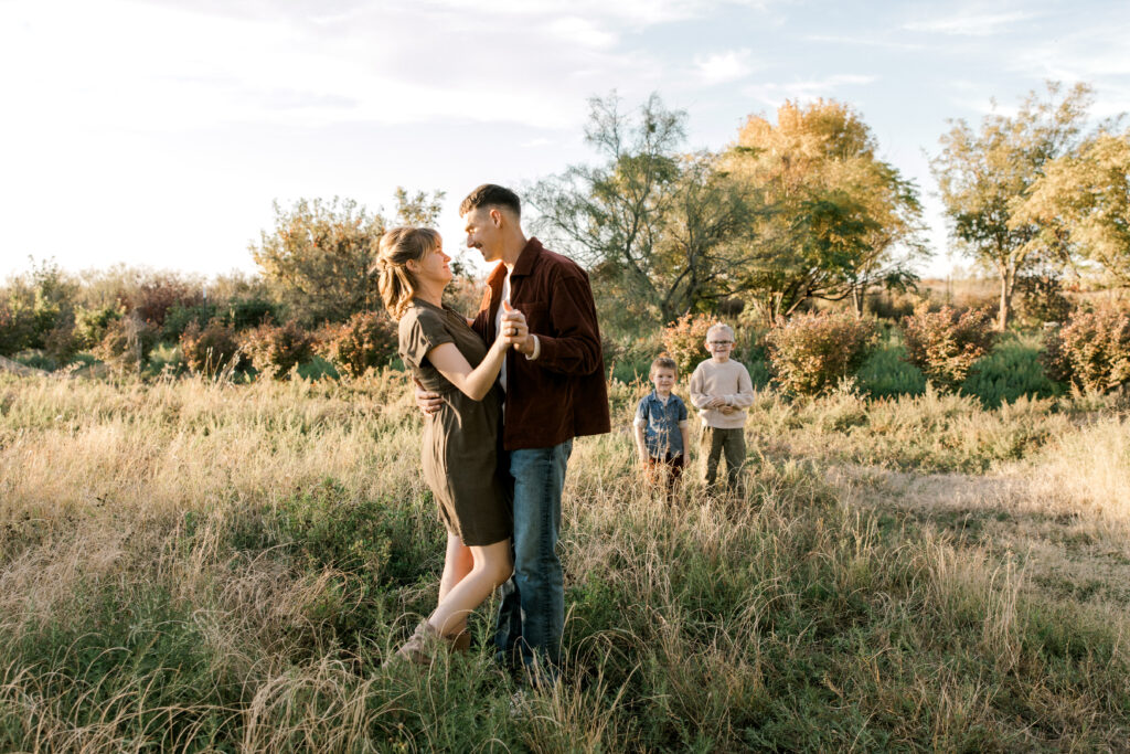 young couple standing in a field with the sunset glowing on them.