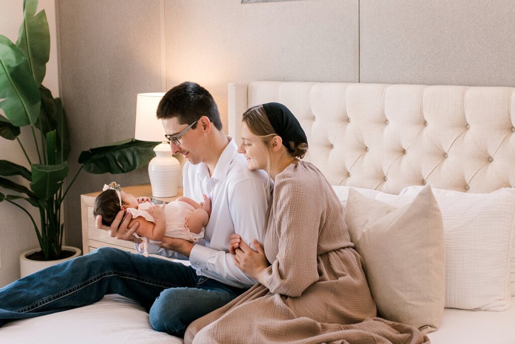 couple sitting on edge of bed looking at baby