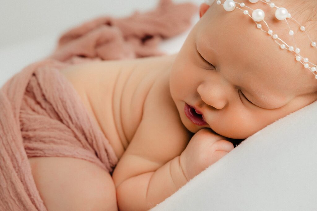 Lubbock newborn photography captured baby in blush pink swaddle laying on white pillows. 