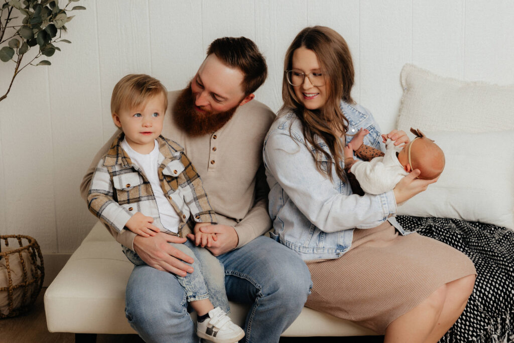 Lubbock newborn photography session captured by Mary Wiebe. The family of four is cuddled up on their couch while mom is holding baby. 