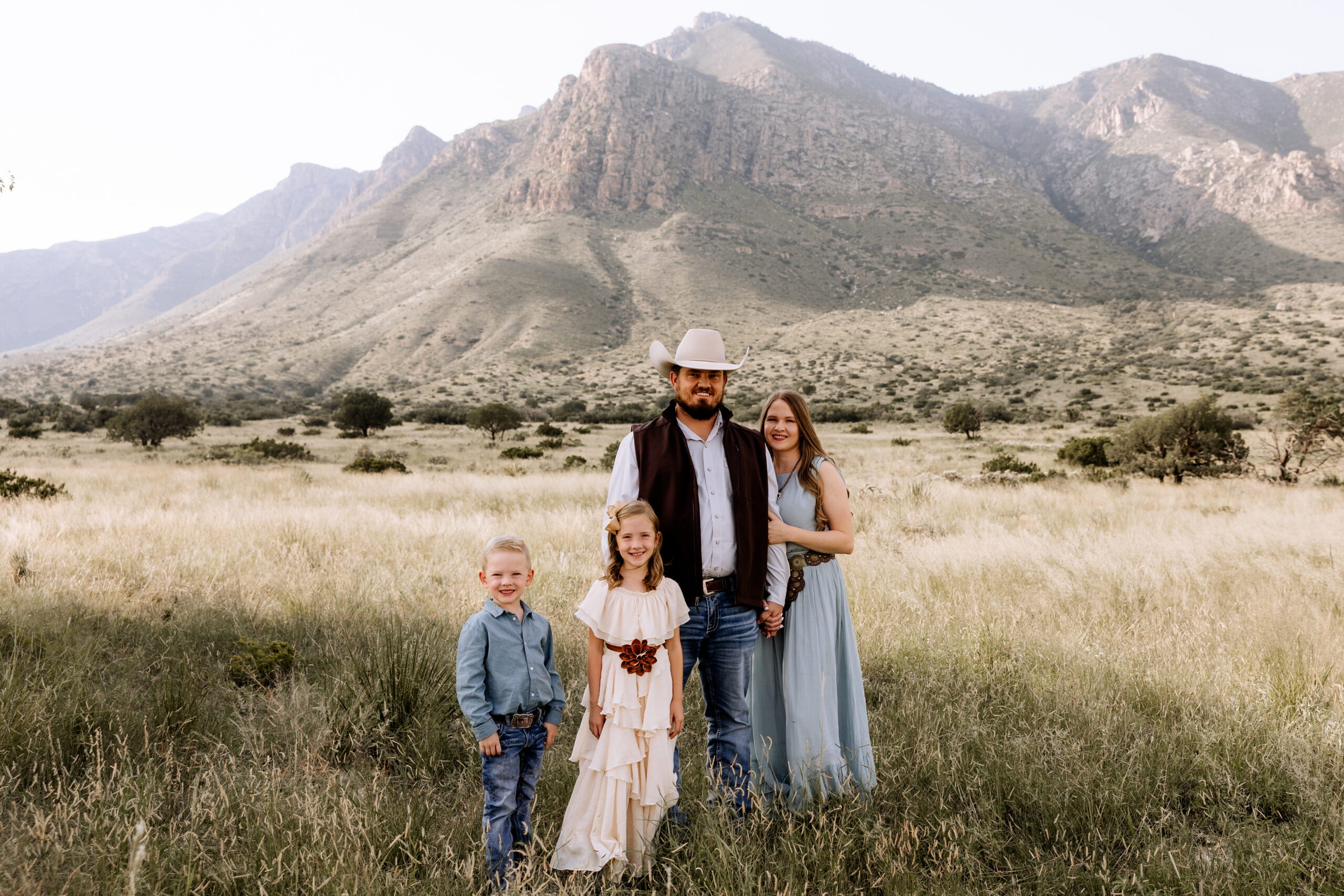 Family of four standing in front of mountains. Mom and dad holding hands while two children are standing in front of them. Captured by Lubbock family photographer, Mary Wiebe.