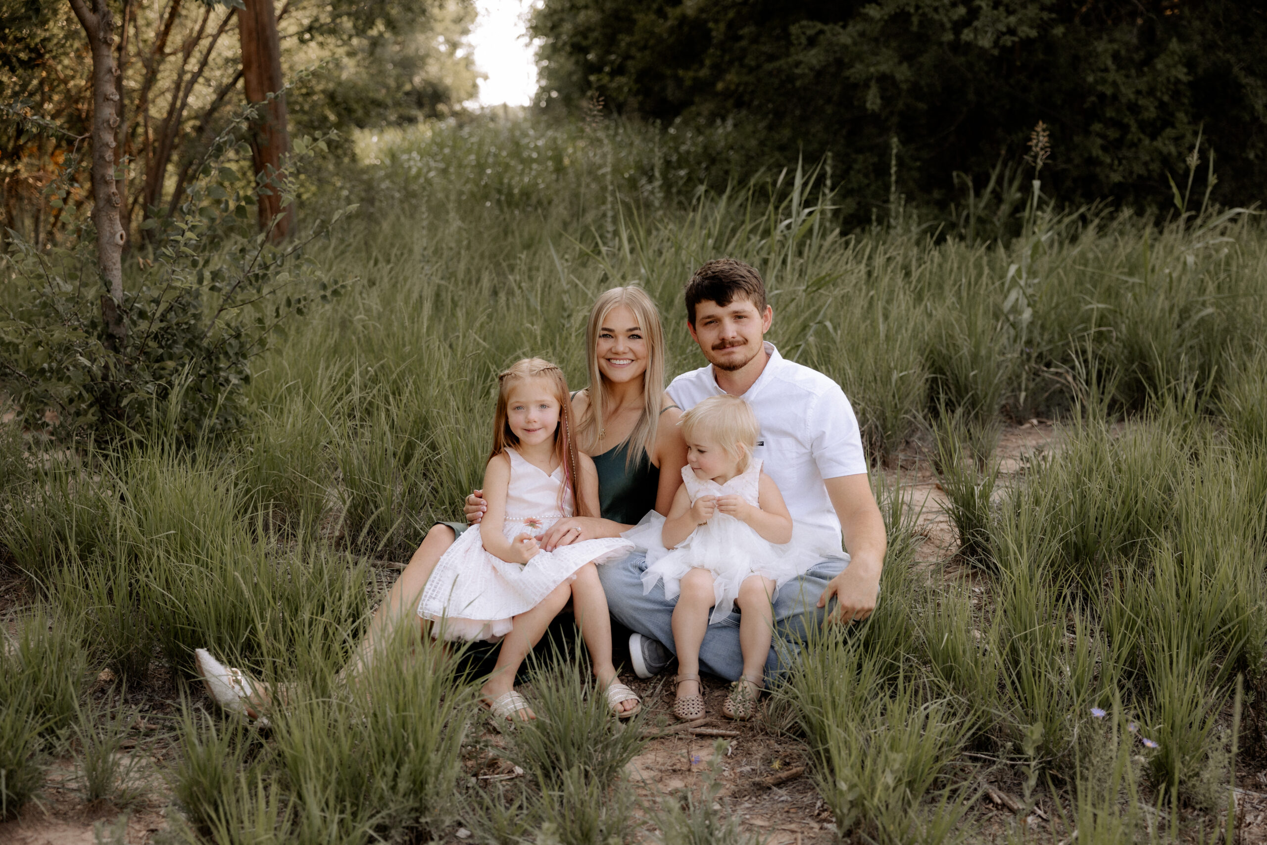 A family, stress-free session captured by Mary Wiebe, a Lubbock family photographer. Family of four sitting on the ground holding each other.