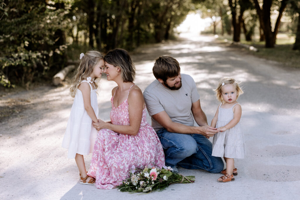 Mary Wiebe captured this family of four; mom, dad, and two daughters are smiling. Mom holding one daughter and dad holding another. Wondering what to wear for spring photos? Wonder no more because Lubbock Family Photographer, Mary Wiebe will guide you. 