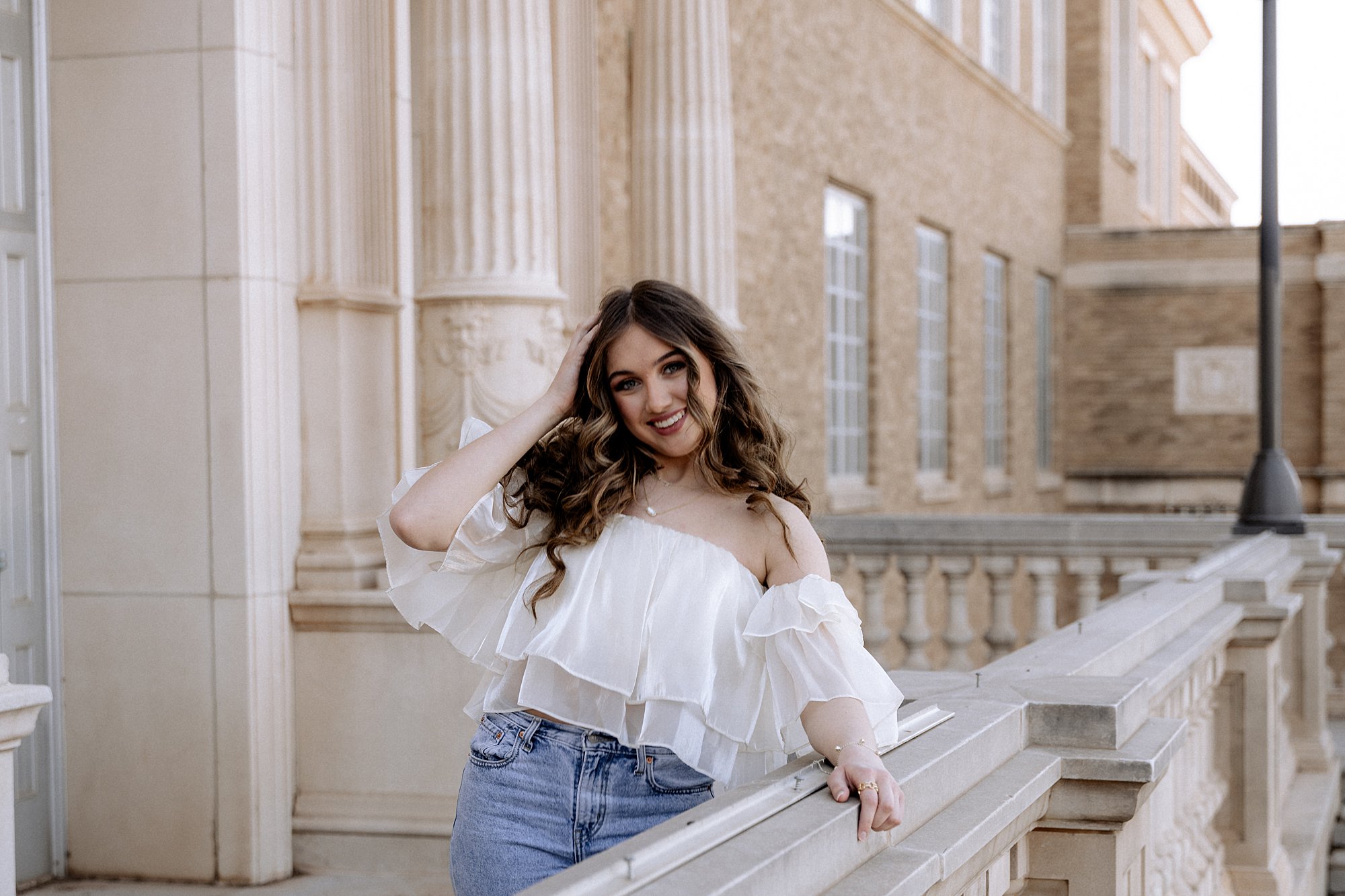 Mary Wiebe, a Lubbock senior photographer, is prompting a senior to hold her hair, lean against the railing and smile ahead.