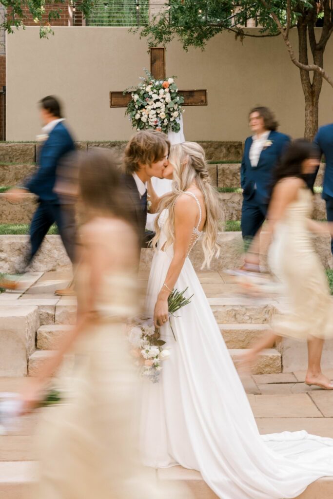 Groom leaning in for a kiss as the bridal party passes by them creating a blurry photo effect. close up of the photo