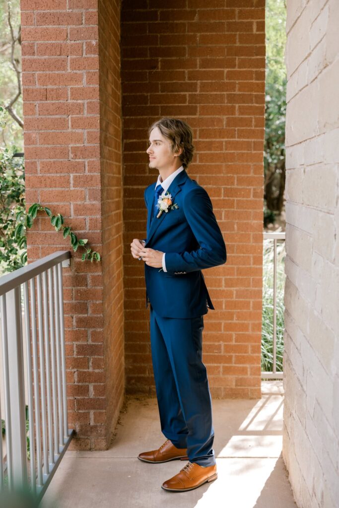 Groom preparing to meet the bride, He is buttoning the top button to his navy suit jacket.