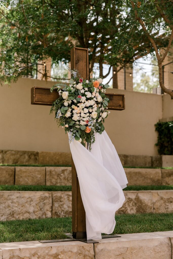 The cross altar at the ceremony location draped in a white linen clothe, adorned with florals, at the Willows in Lubbock Texas