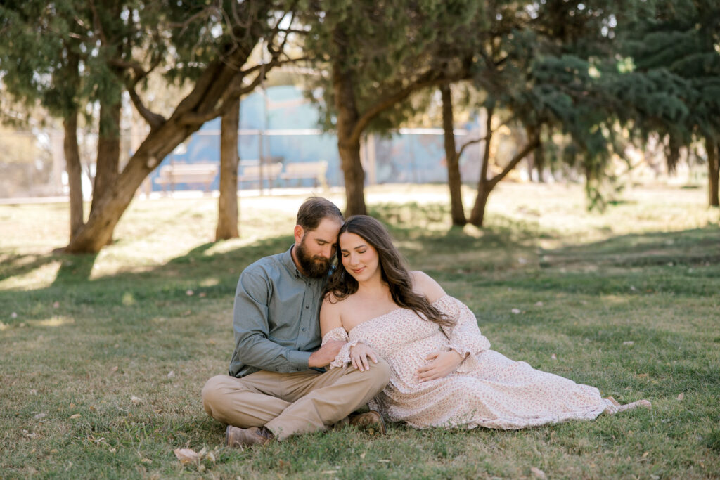Couple sitting on the ground holding each other during their spring maternity session. Captured by Mary Wiebe Photography in Lubbock, Texas. 