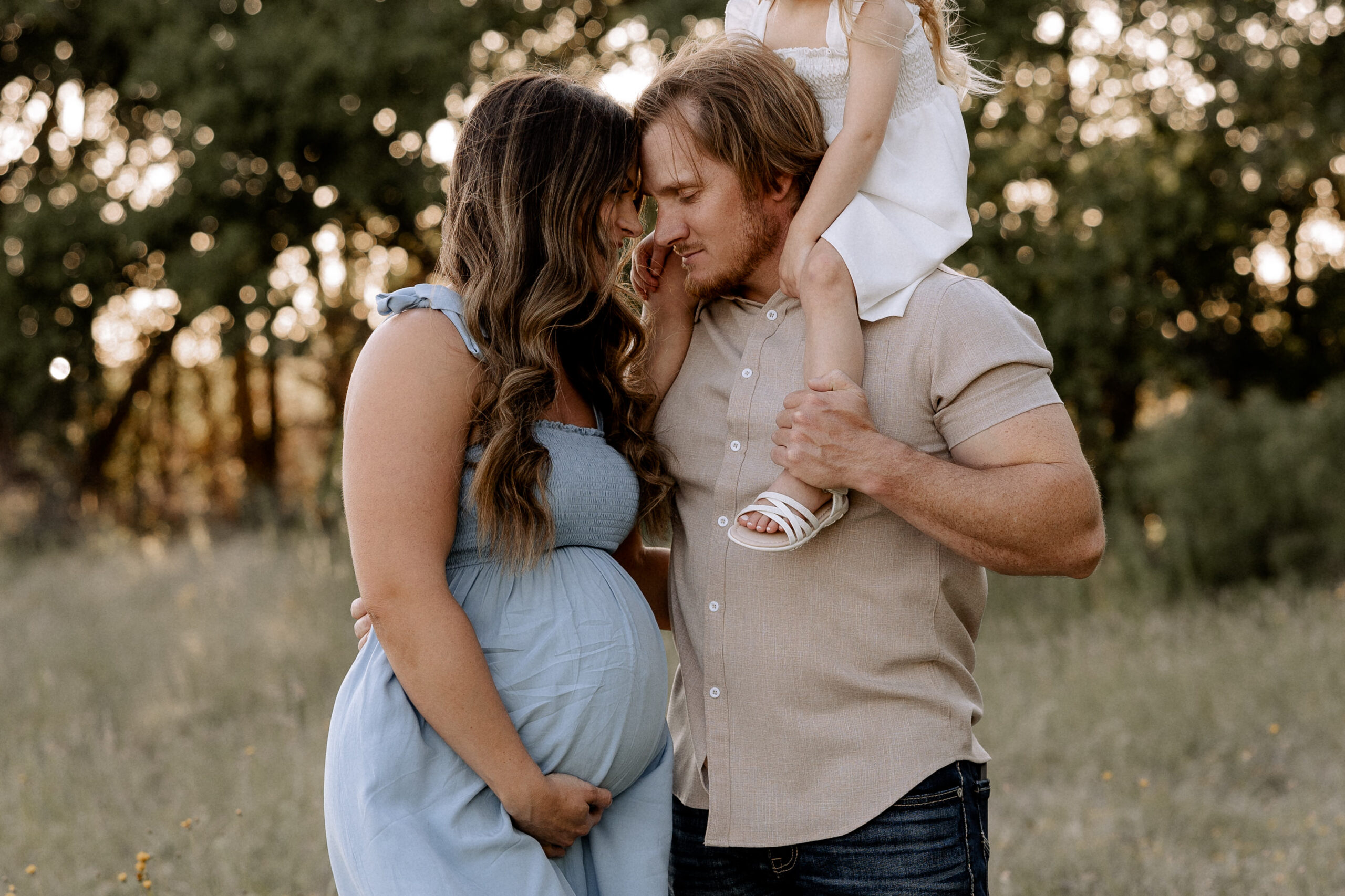 Mary Wiebe answers all your questions about what to expect at your maternity session. In the photo, mom, dad, and little girl are in the photo with mom and dad leaning their heads together.