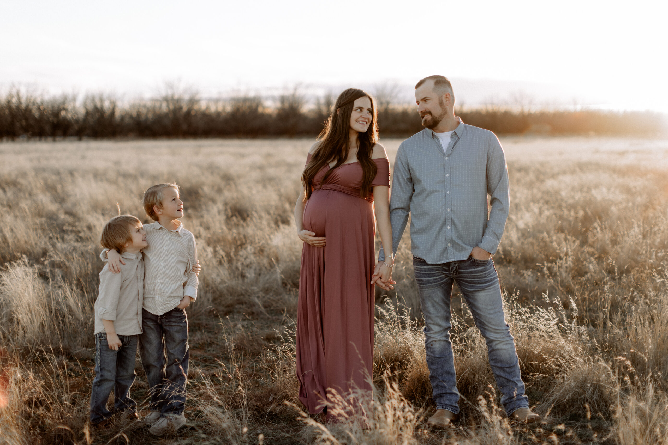 It is worth capturing every pregnancy. In this maternity session the mom and dad are holding hands, and their two little boys are smiling up at them from a few feet away. Captured by Mary Wiebe Photography.