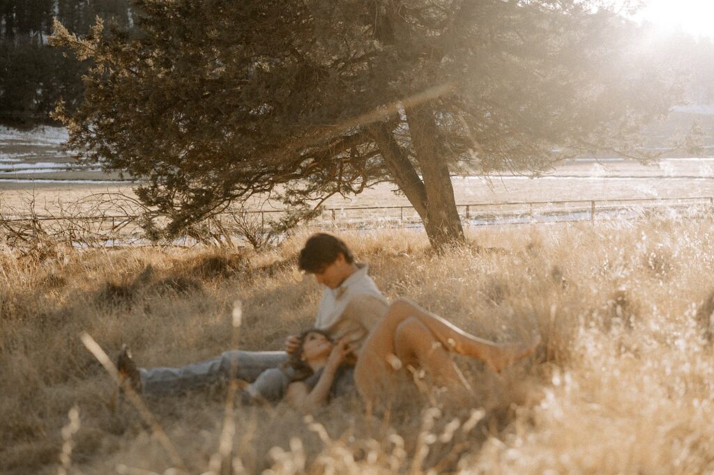 Here a couple is laying under a tree with the girl laying on his lap and he is holding her. Captured by Lubbock Engagement Photographer, Mary Wiebe. 