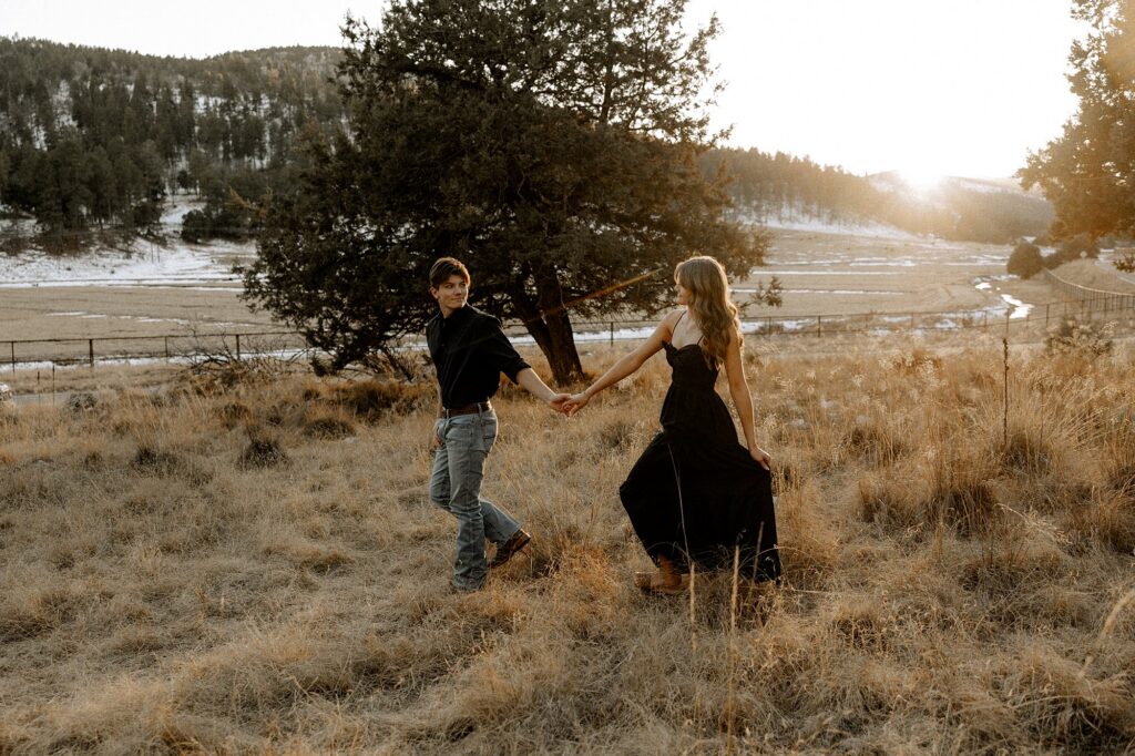 Couple is holding hands walking through tall grasses. Captured by Mary Wiebe Photography. 