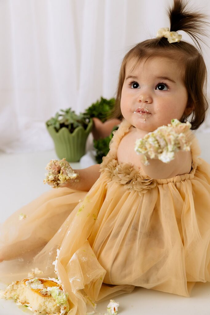 While doing a cake smash photo session, this little girl is looking up with a mouth full of cake!