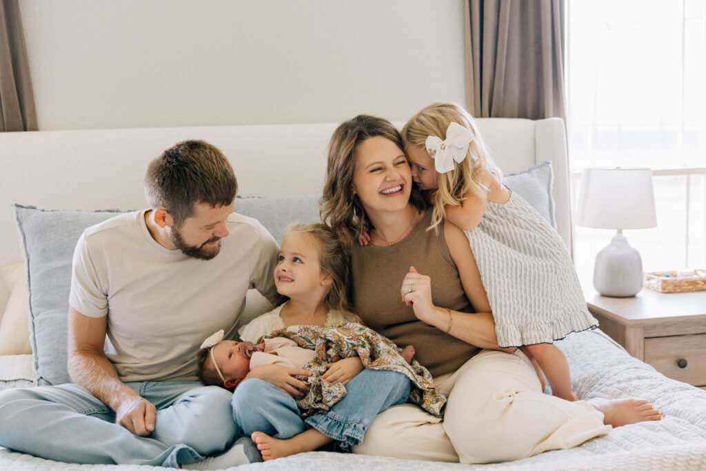 This lifestyle newborn sessions in Lubbock was captured by Mary Wiebe Photography. In the image a new family of 5 is sitting on the parents' bed. 