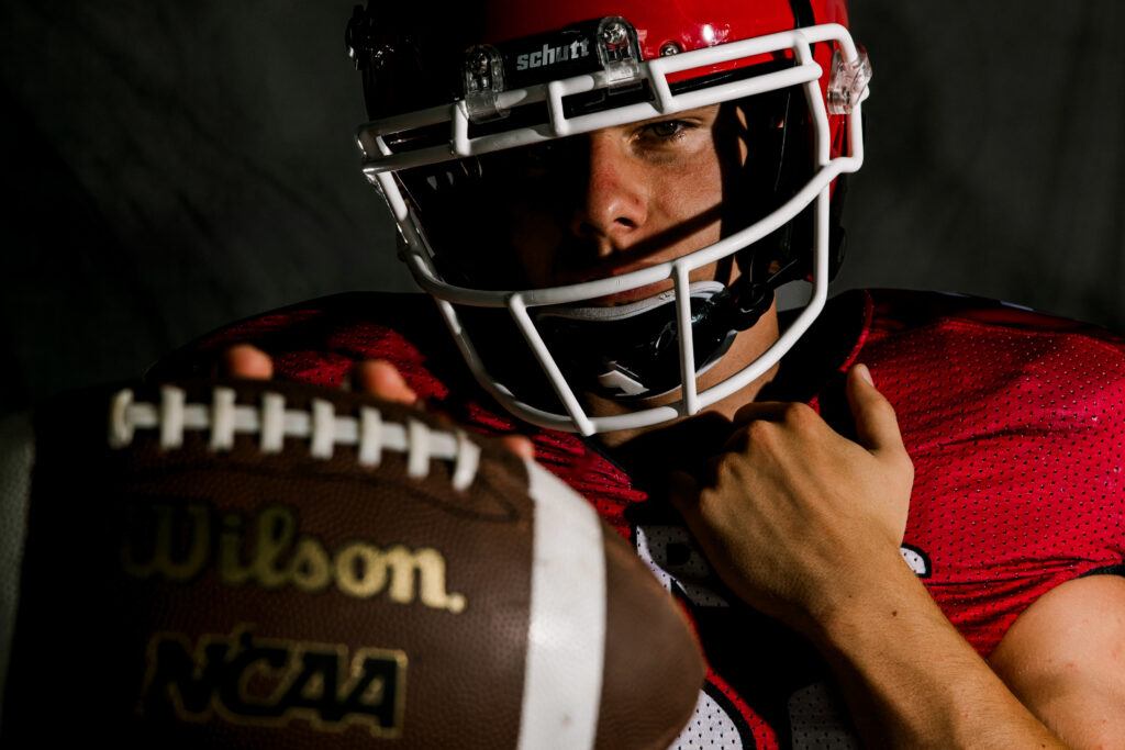Athlete senior pictures taken by Mary Wiebe Photography. Here a senior football player is holding the ball to the camera.