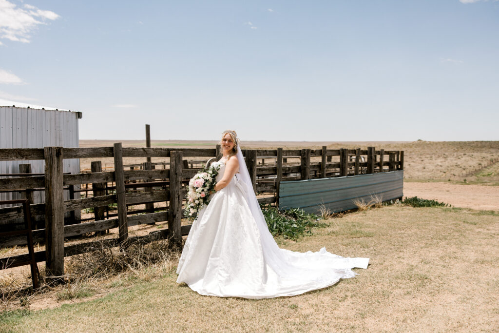 Bridal portraits in Texas captured by Mary Wiebe Photography. Here the bride is standing alone by a wooden fence.