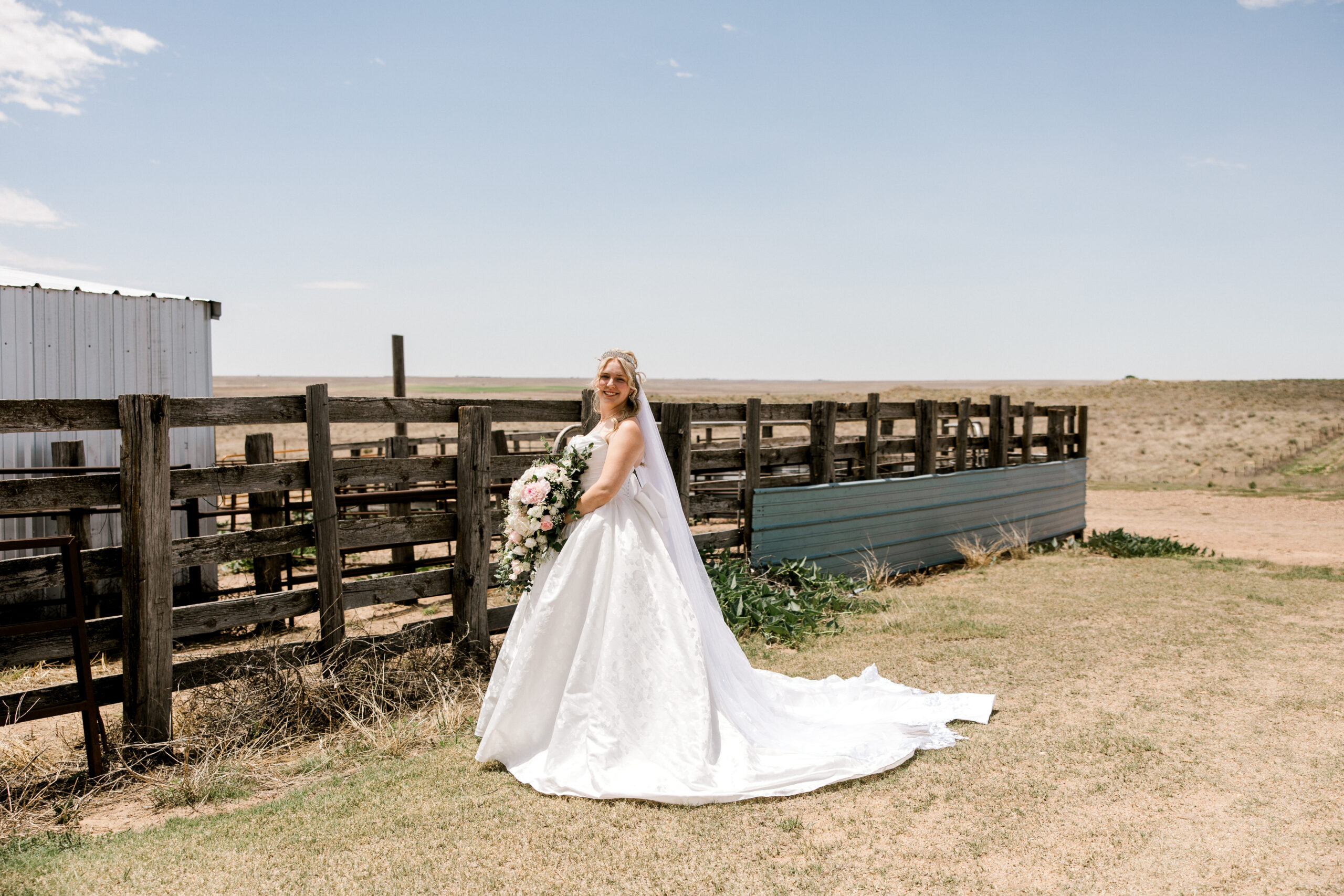 Bridal portraits in Texas captured by Mary Wiebe Photography. Here the bride is standing alone by a wooden fence.