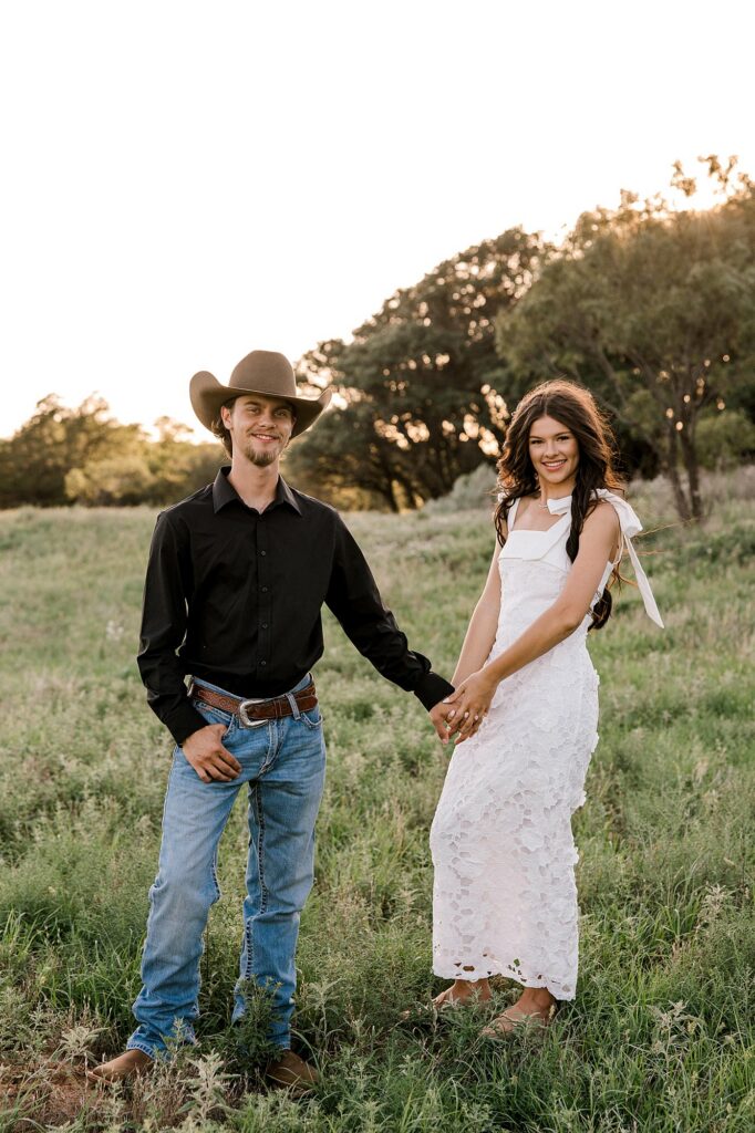 Here a future bride and groom are holding hands and looking at the camera during golden hour. 