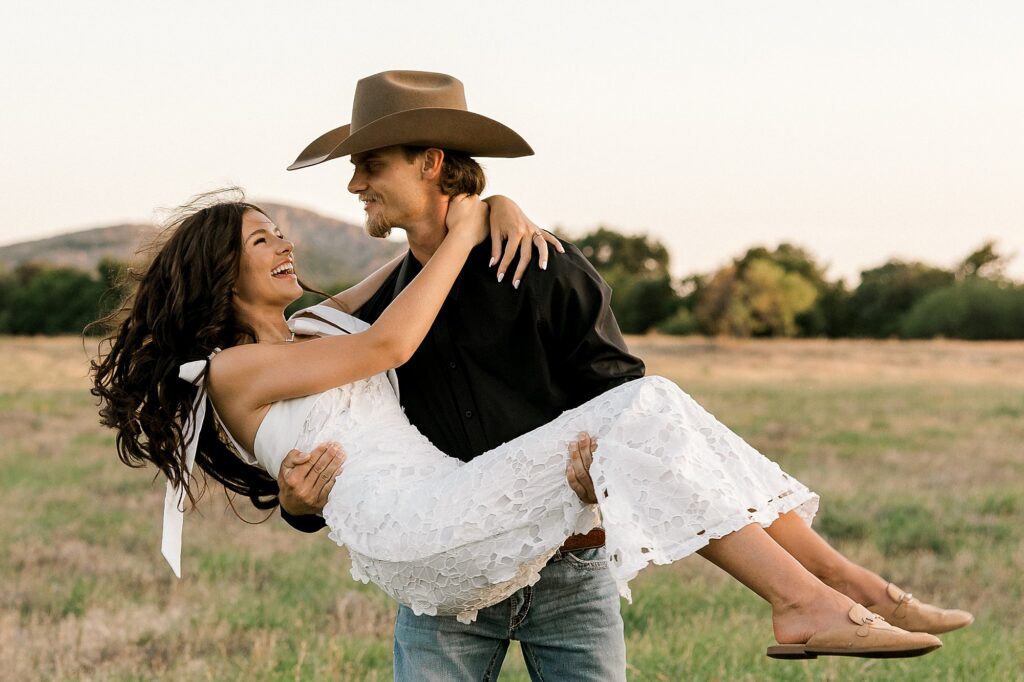 Young man holds his future bride and spins her around while she laughs. Captured by Mary Wiebe Photography. 