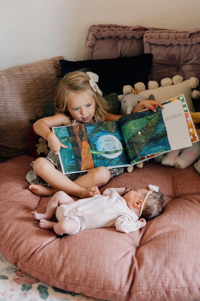 Little sister reading to her newborn sister. 