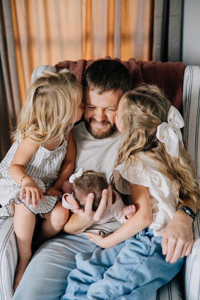 A father and his three daughters are sitting on a chair together. 