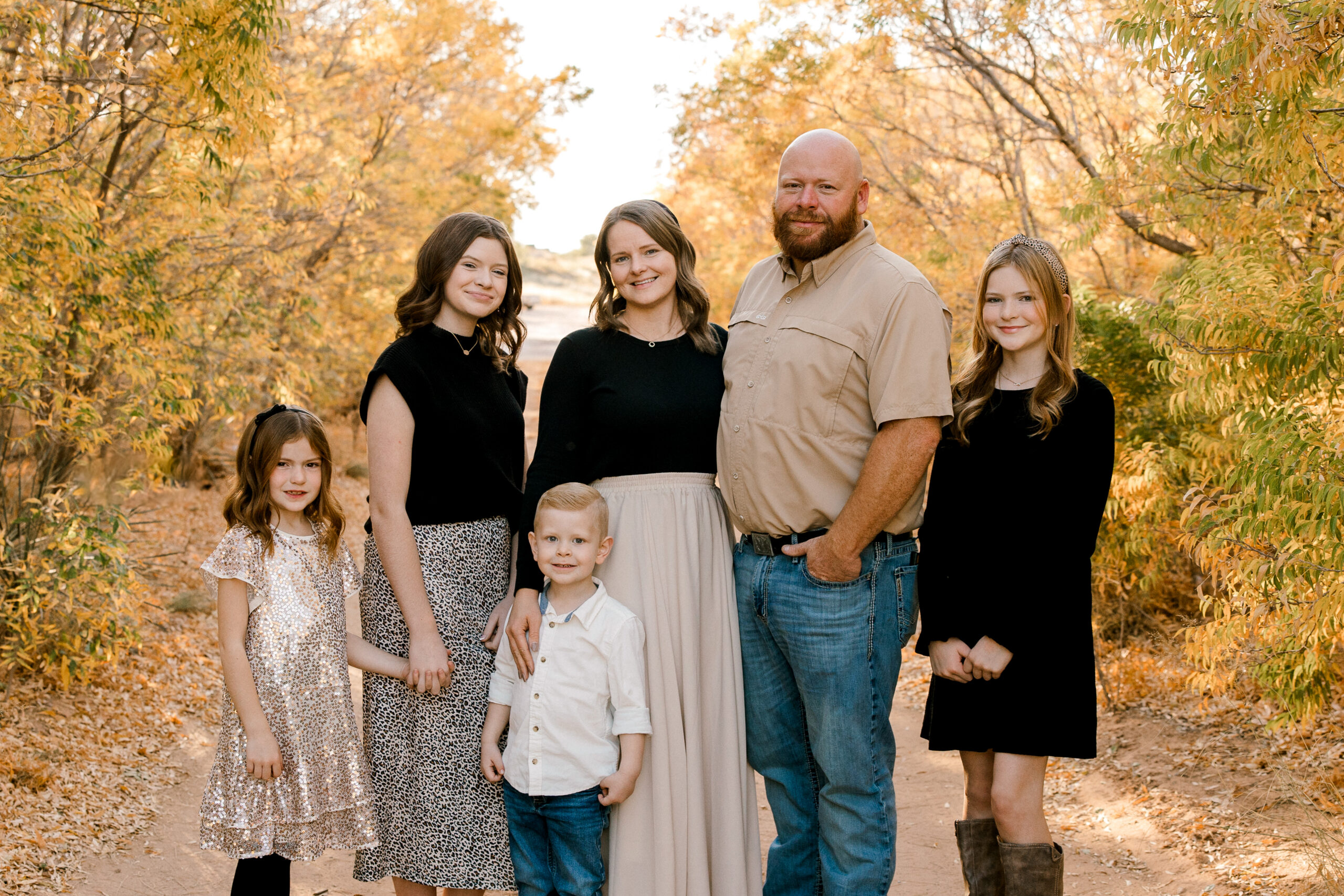 Learn about all the best fall activities in Lubbock! Here a family of 6 is standing in a shaded area with lots of fall colored trees.