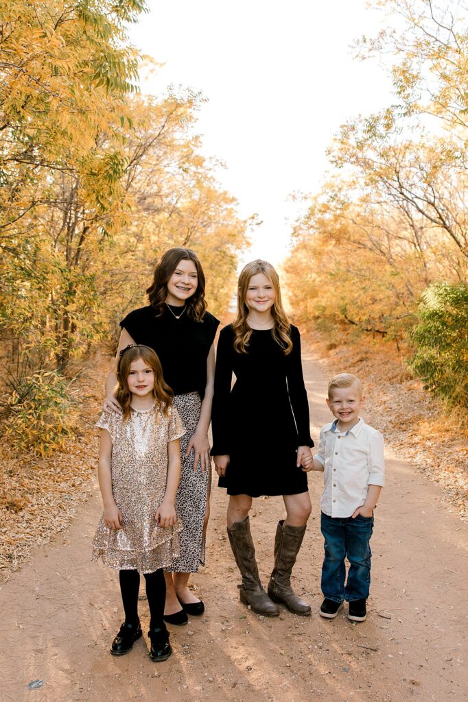 Four children standing on dirt road in fall foliage season. 