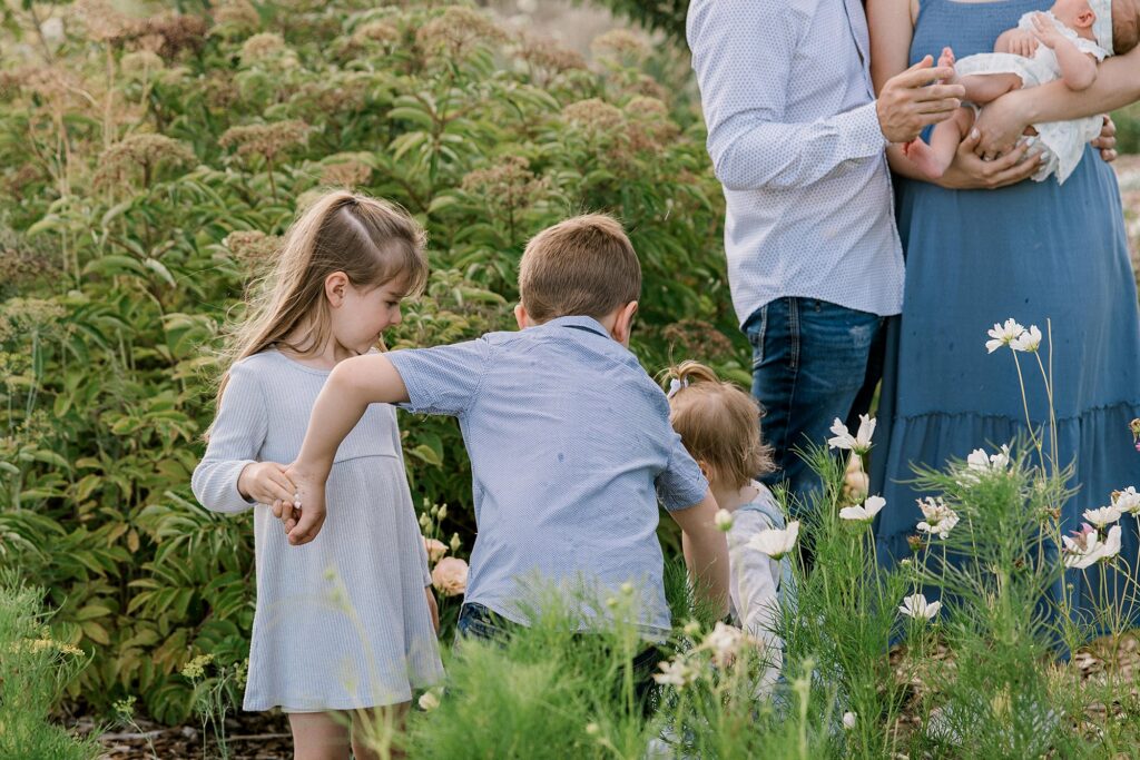 Three small children playing in a field of green grass and flowers.
