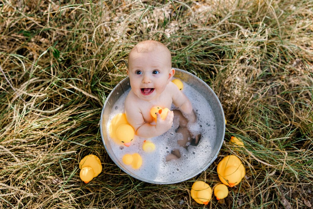 Baby boy looking up at the camera with rubber duckies in hand smiling. 