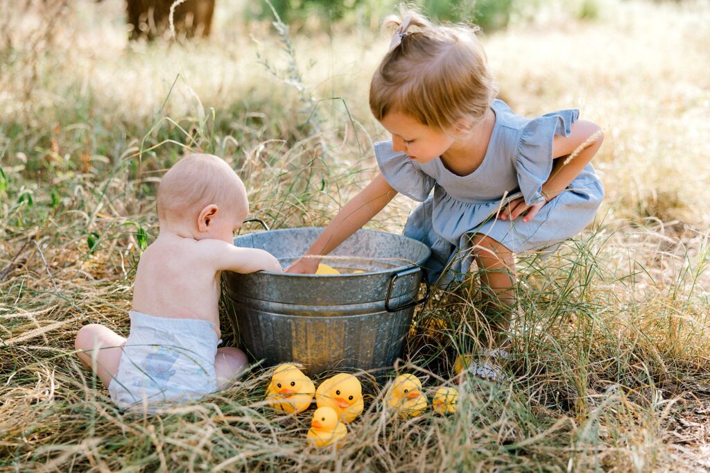 Baby boy and big sister are playing in a bucket of water outside. 