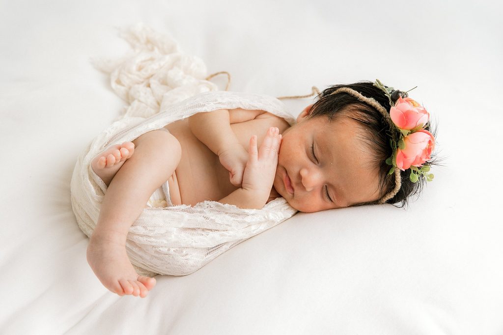 Newborn baby girl sleeping soundly on a while blanket. 