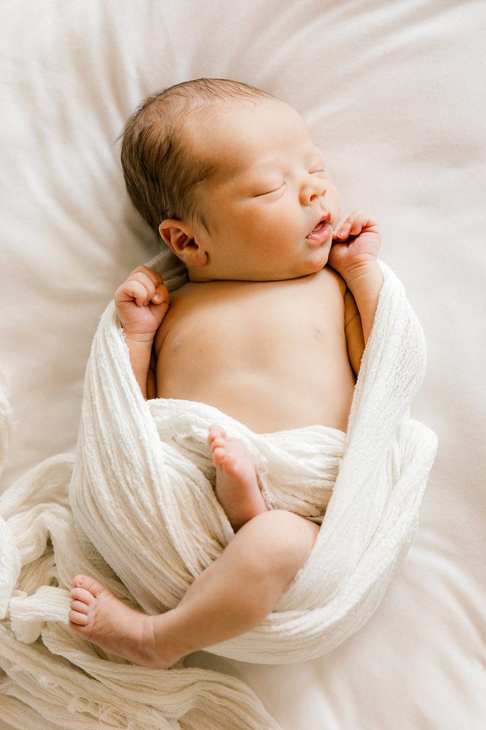 Newborn baby boy in swaddles sleeping away on a white bed.