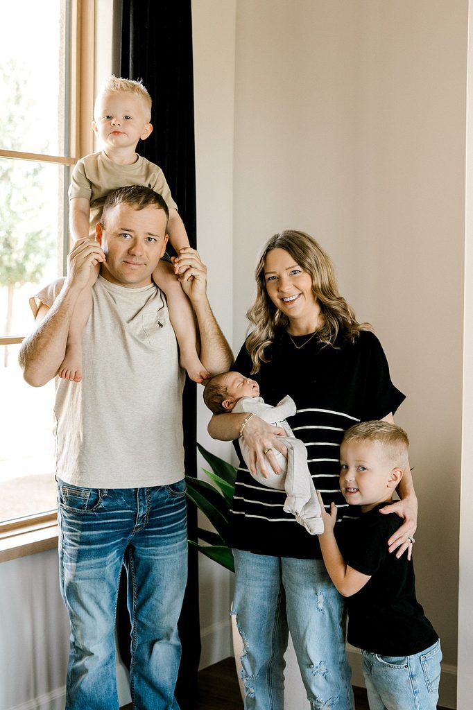 Window-lit nursery prepared for a newborn photo session in Midland, TX. Family standing and smiling.