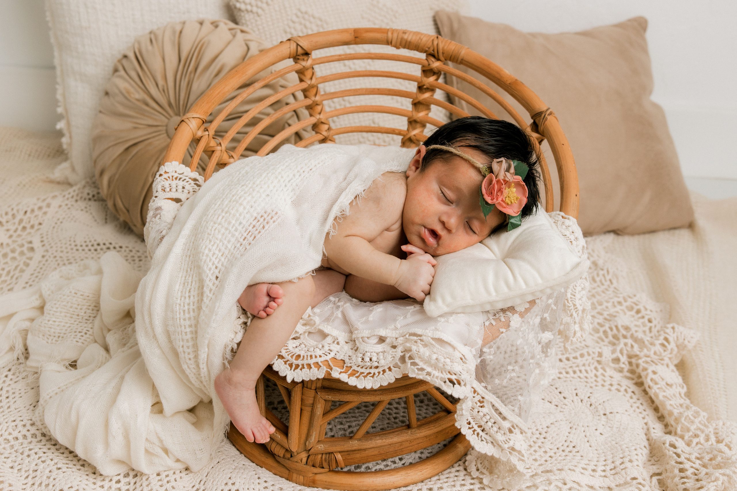 Newborn girl laying on pillow, with white swaddles laid across her. Learn how long a does a newborn photography session take in this blog by Mary Wiebe Photography.