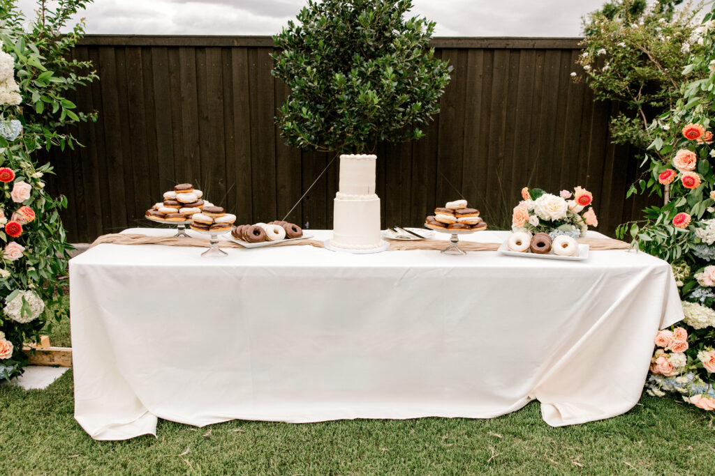 Wedding dessert table with a white cake, donuts, blush flowers, and neutral linens showcasing a soft wedding color palette