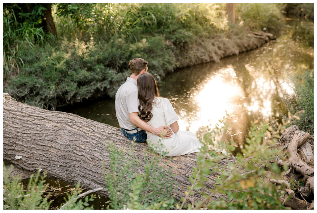 Engaged couple sit on a tree trunk and look over the glowing creek below