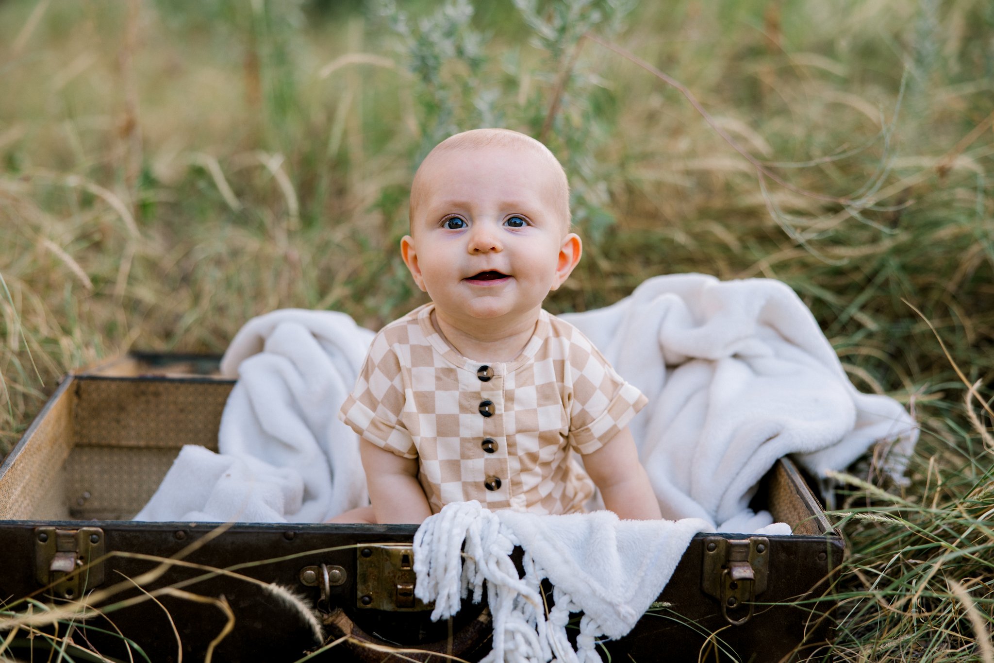 Six month old baby boy sitting on a blanket, smiling at the camera.