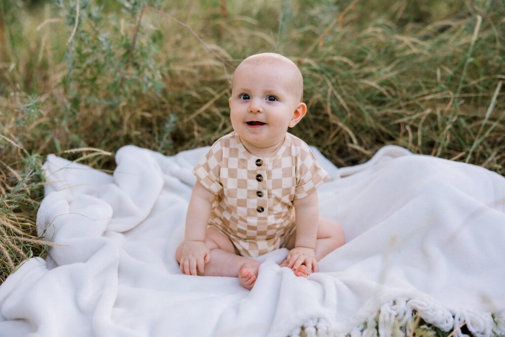 Little boy sitting on a blanket smiling at the camera.